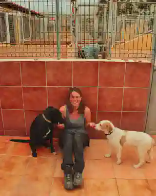 Jo sitting laughing next to two dogs while feeding them.