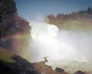 Jo sits at the Taennforsen waterfall and enjoys the refreshing mist. You can see a rainbow above the waterfall