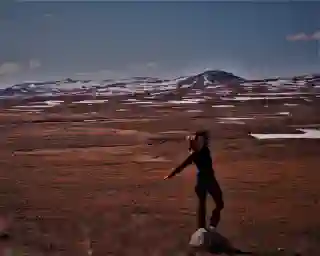 Jo in der Wüste Vildmarksvägen. Im Hintergrund Berggipfel mit Schnee, alles ist in rötliches Licht getaucht.