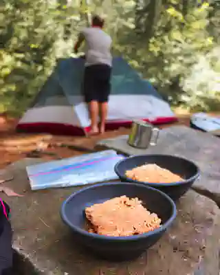 Two bowls in the foreground with pasta in tomato sauce. In the background Georg sets up the tent