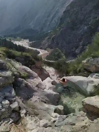 View into the valley with a refreshing bath. You can see the Partnach  river. In a small pool, Georg is sitting and looking into the valley.