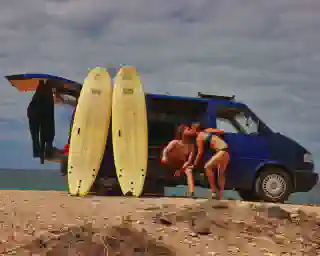 Die Quest am Strand, an ihr lehnen zwei große Surfbretter und Jo und Georg in Badekleidung 