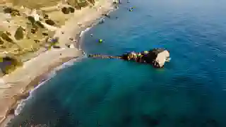 Küste mit Sandstrand. 
Das Meer ist dunkelblau und ein Fels steht in der Brandung.
Die Quest, der kleine blaue Van, steht auf dem Strand.
