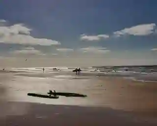 Ein langer Sandstrand und im Hintergrund das Meer. Zwei Surfbretter liegen umgedreht am Strand