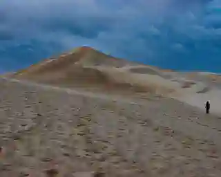 Gray sky over the sand dune, with Jo walking through the sand in the lower right