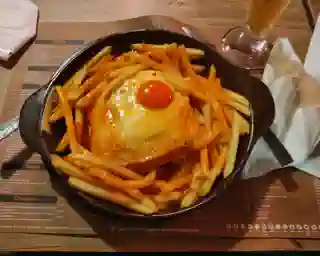 A small cast iron pan with the Francesinha, topped with a fried egg. The sandwich is usually served with French fries