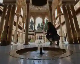 Ein Garten in der Alhambra. Man sieht viele Säulen und einen kleinen Brunnen im Vordergrund