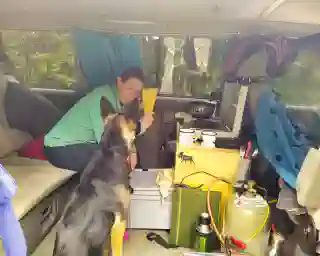 A view through the side door into the bus. Jo and Momo are inside, cooking spaghetti.