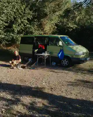 Our van life test. A green VW T4. In front of it, a table and two chairs, and a smiling Georg.