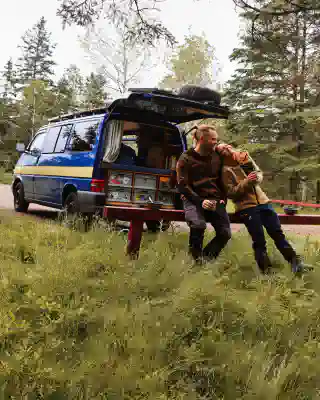 Jo und Georg sitzen hinter dem Van, der "Quest". Die Heckklappe ist offen und Jo hat sich an Georg angelehnt.