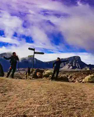 Georg, Jo, and Momo in the Teide National Park at a signpost. Jo points in one direction, and Georg points in the other.