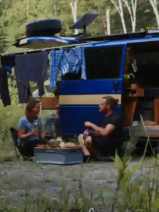 Jo and Georg sit in front of the open sliding door with a table and chair, enjoying a meal. Behind them, a clothesline is stretched.