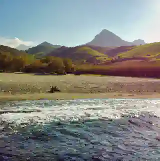 Erste Nacht zurück im Van nach dem Volunteering. Vorne sieht man das Meer, dahinter Strand und die Quest. Georg und Jo sitzen am Strand. Ganz in der Ferne ist ein Berg zu sehen