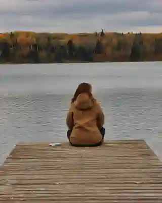 Jo is sitting on a jetty at a lake. On the other shore an autumnal forest