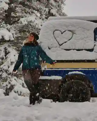 Jo in the snow in front of the van. A heart is drawn in the snow on one of the windows.